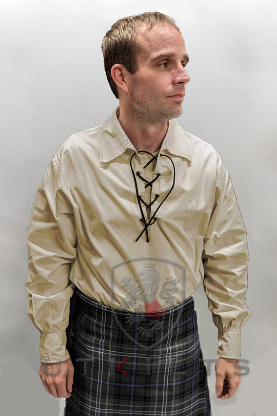 A man wearing a kilt and shirt stands confidently, showcasing traditional Scottish attire.