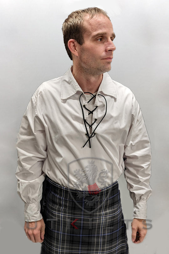 A man wearing a kilt and shirt stands confidently, showcasing traditional Scottish attire.