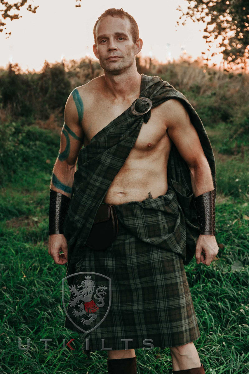 A man wearing a Great Kilt stands confidently in a vibrant field, embodying cultural pride amidst the natural landscape.
