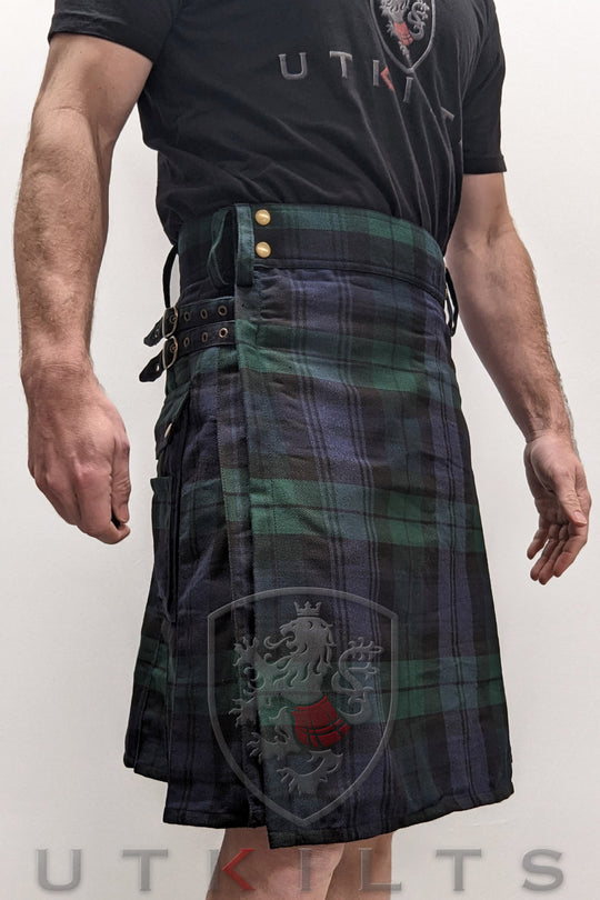 A man in a kilt, complemented by a black shirt presents a striking and fashionable appearance.