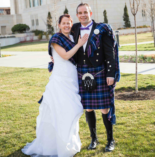 A man and woman in kilts smile for a photo, featuring special order tartan fabric, fly plaids, sashes, and neck ties.