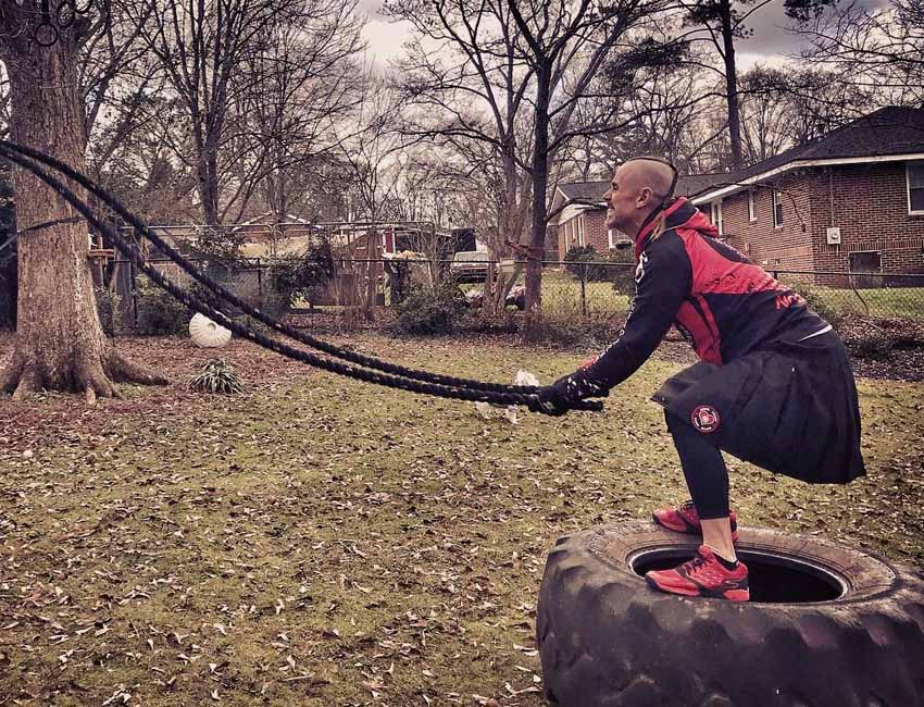 An athlete in a red jacket and black pants grips a rope, showcasing strength and determination in his stance.