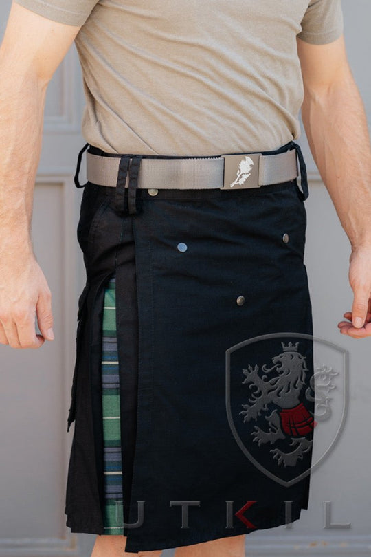 A man wearing a kilt stands confidently in front of a wooden door.