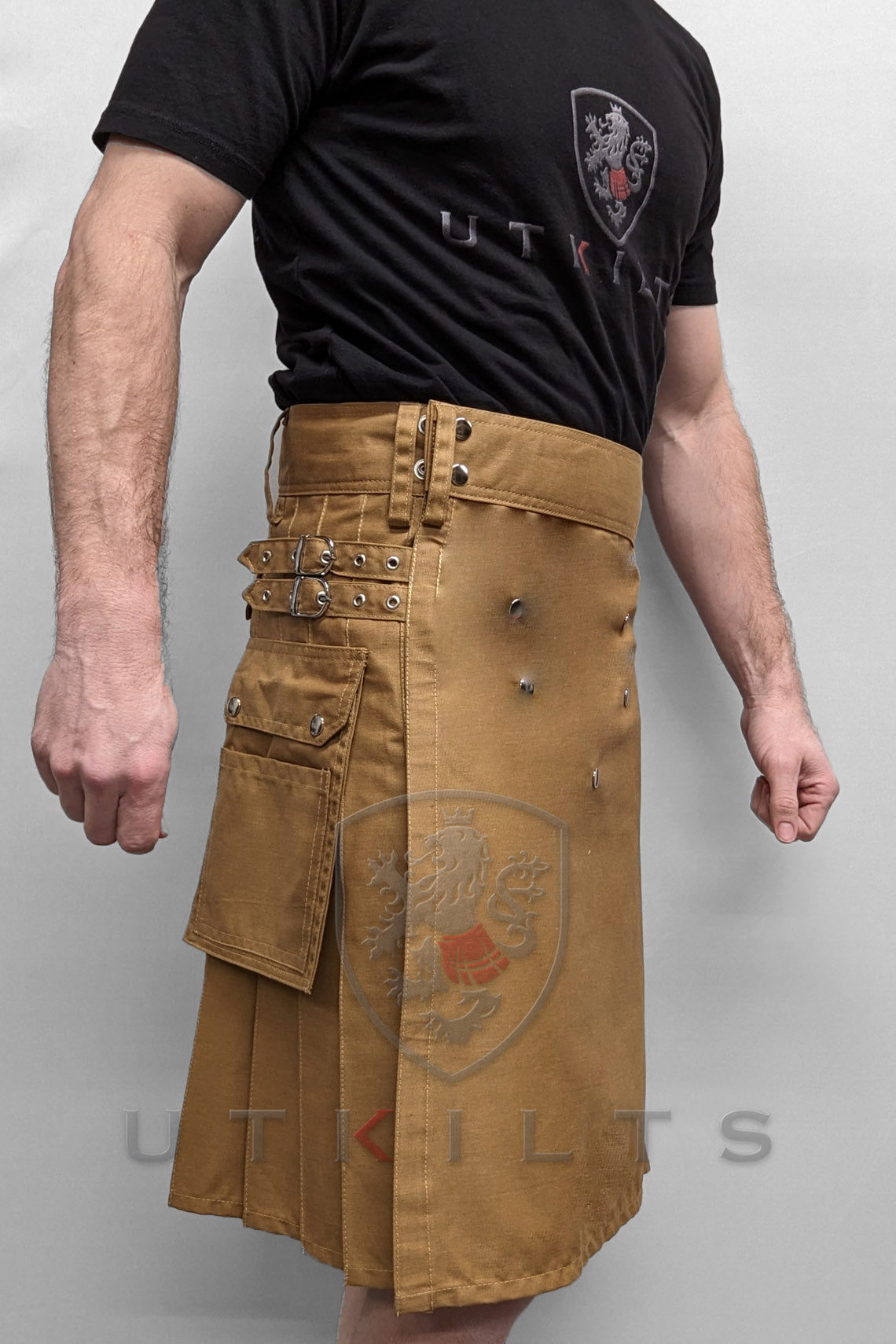 A man showcases a deluxe dark khaki utility kilt with rivets, emphasizing its fashionable and functional design.