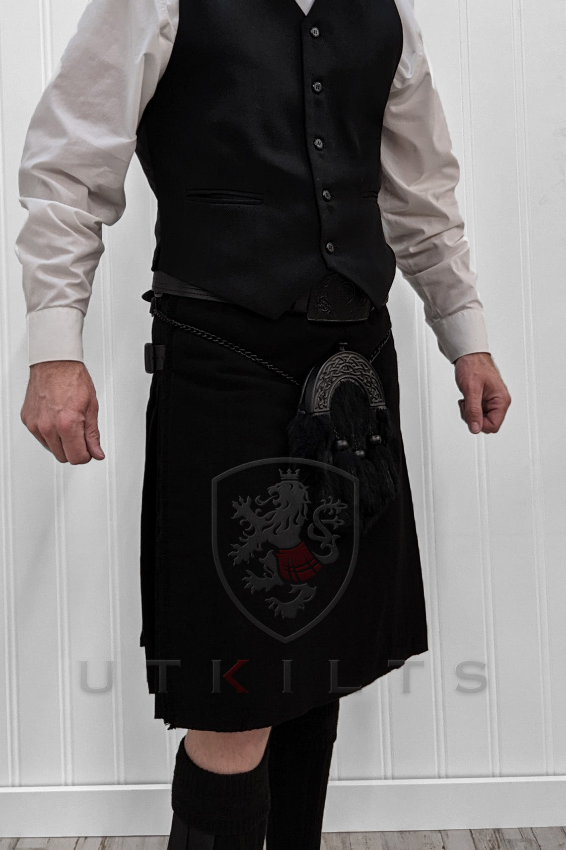 A man wearing a premium solid black wool tartan kilt stands with arms crossed, showcasing a strong and confident demeanor.