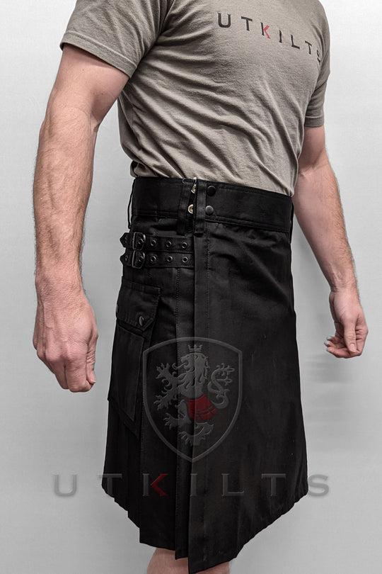 A man dons a standard black utility kilt presenting a contemporary and stylish appearance.