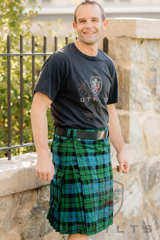 A man dressed in a kilt paired with a black shirt, standing confidently in a casual setting. 