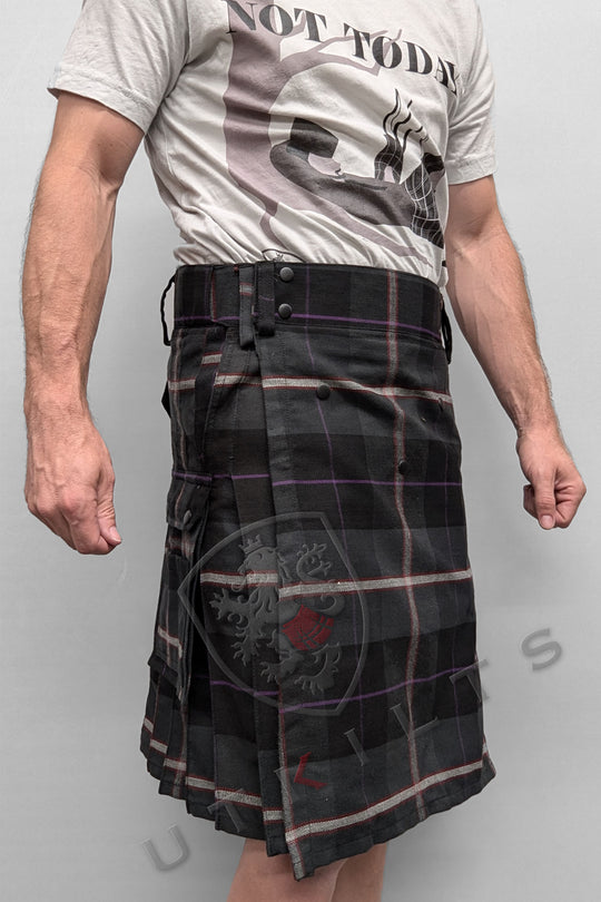 A man dons a black and purple tartan kilt, featuring the Ultimate Midnight Sea Tartan Utility Kilt with a comfortable waist design.