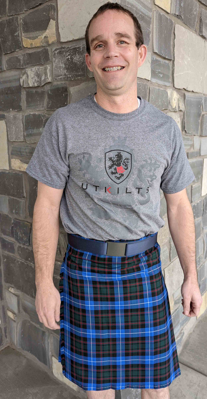 A man dressed in a Scottish 4-yard kilt with a blue belt, representing traditional Scottish fashion and craftsmanship.