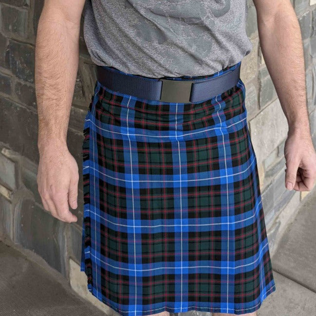 A man dressed in a blue and black tartan kilt, showcasing traditional Scottish attire with confidence and style.