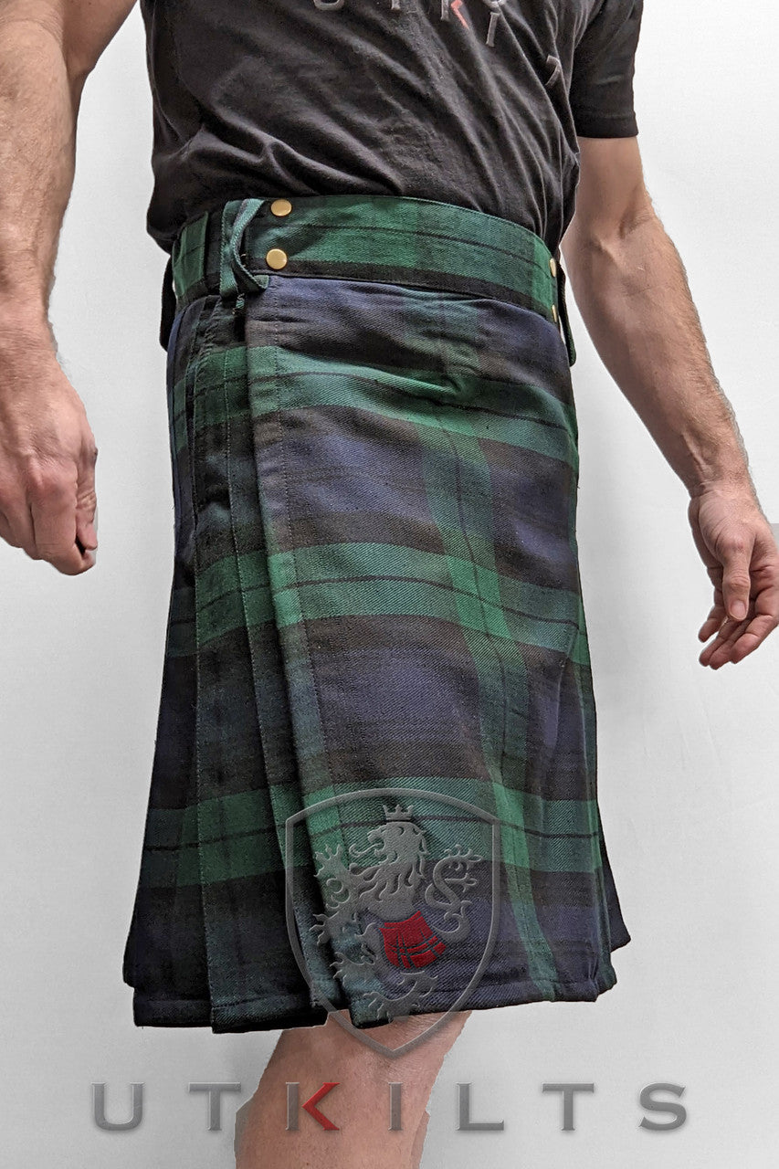 A man displays the front side of a Business Edition Ultimate Black Watch Tartan Utility Kilt.