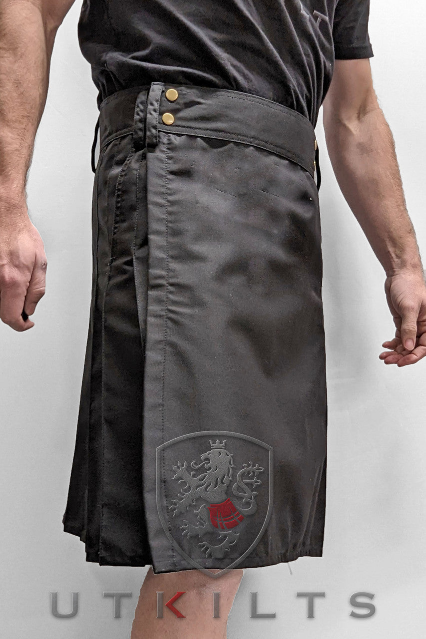 Front view of a man dressed in a black utility kilt adorned with a red badge, representing the Business Edition Standard style.
