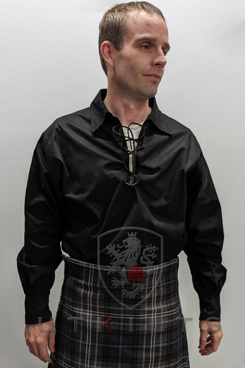 A man wearing a black Jacobite Ghillie shirt and a plaid kilt, showcasing a traditional Scottish attire.