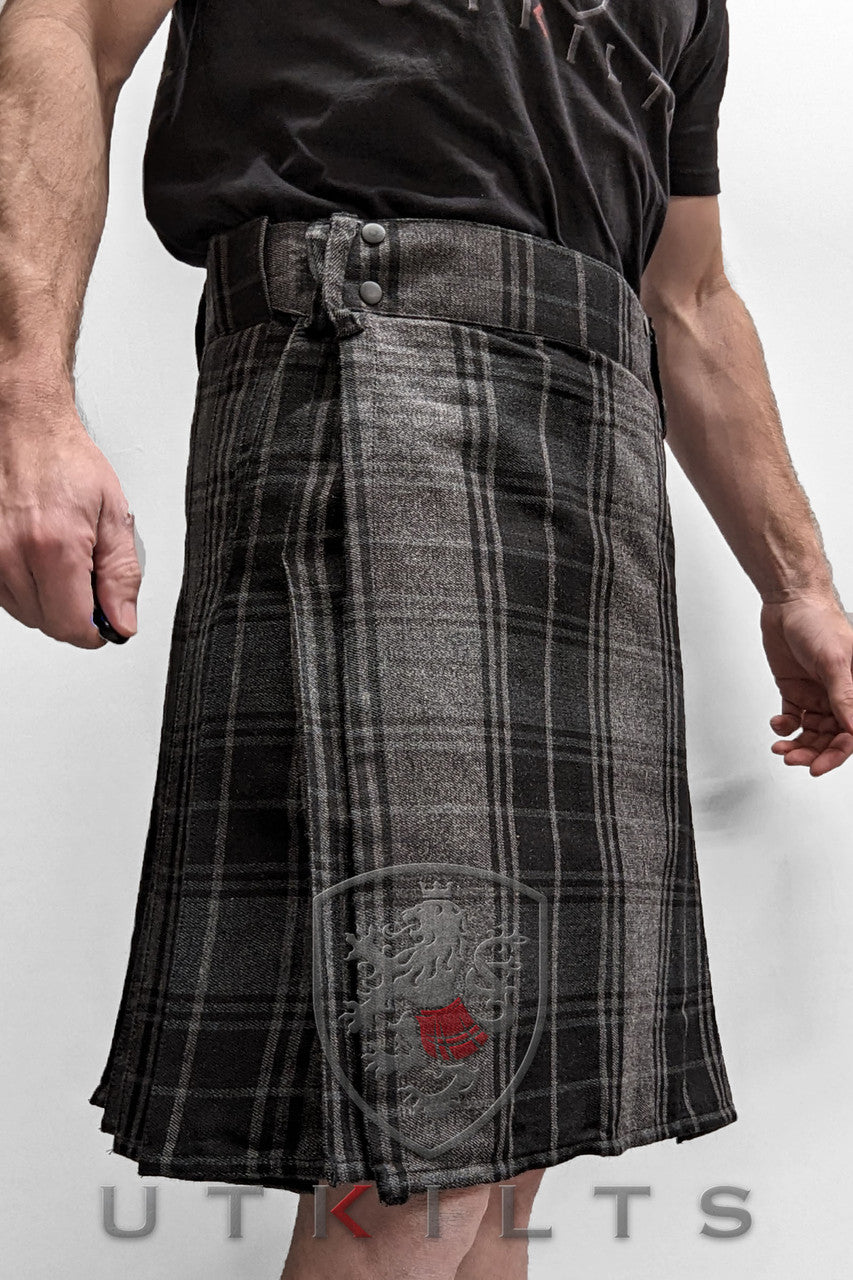A man in a black and grey tartan kilt, showcasing the front side of the Business Edition Ultimate Highlander Gray Utility Kilt.