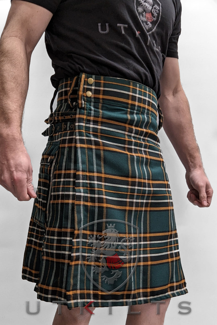 A man proudly wears a green and orange tartan kilt, showcasing the Standard Irish Heritage Tartan Utility Kilt design.