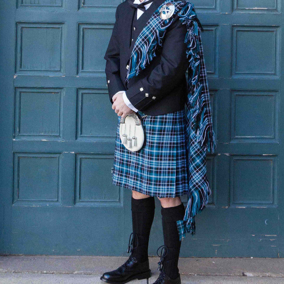 A man wearing a kilt poses in front of a door, highlighting the Argyll Formal Kilt Package available from $299.50.
